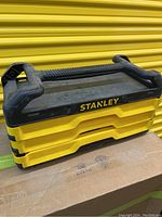 Closed 3-drawer yellow and black Stanley tool chest with a black handle immersed on a cardboard box background.