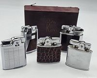 Front view of five vintage lighters with distinctive designs and one dark brown Ronson box