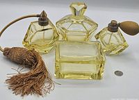 Photo of the full yellow glass Art Deco style dressing set showing two atomizer perfume bottles, one marked Homespray, one stopper perfume bottle, and a rectangular dish, all in yellow glass with metal and fabric pump parts