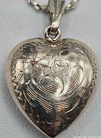 Close-up of the vintage sterling silver heart pendant showing detailed engraved floral patterns.