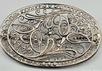 Close-up view of the front of the oval-shaped filigree brooch showing intricate silver scrolling patterns.