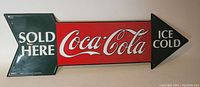 Front view of the Coca-Cola advertising metal sign with arrows and text