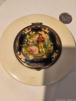 Closed compact showing decorative painted lid panel with romantic vintage scene and scrollwork.