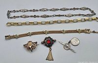 Photo showing two metal bracelets and three brooches/pins arranged horizontally with a dime for size reference.