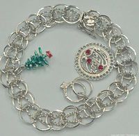 Full view of silver chain-link bracelet with three charms laid out to show the details of each charm.