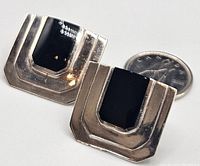 Close-up photo of one sterling silver rectangular earring with polished black onyx stone, showing size reference next to a Canadian quarter coin.