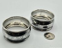 Two vintage Birks sterling silver napkin rings next to a Canadian quarter for size reference, showing the exterior surfaces with reflective tarnish and wear.