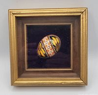Front view of a vintage Ukrainian hand-painted Easter egg displayed in a gold-tone shadow box frame with a dark mat background.