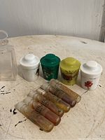 Photo of four vintage conical perfume solid containers and six small glass perfume vials on a white chipped surface