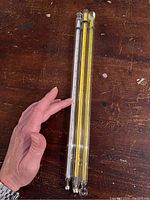 Full view of three glass scientific thermometers held against wood surface, showing length and form