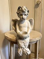 Front view of white composite angel shelf sitter figurine holding tea light candle holder with seashell hair detail.