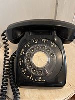 Front view showing black rotary dial telephone with white alphanumeric markings and crack in dial center.