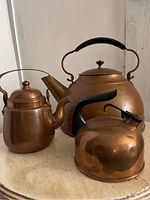 Three copper kettles grouped together on a flat surface showing overall size and condition.