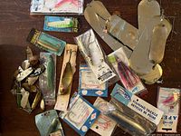 Overview photo of multiple fishing lures and tackle laid on wooden surface including spoons, spinnerbaits and hard lures, some new in packages