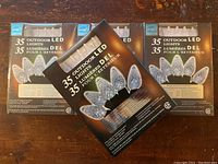 Four unopened boxes of 35-count outdoor LED Christmas light strings stacked on a wooden surface showing packaging and bulbs.