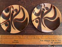 Two round enamel dishes with abstract butterfly design in brown and copper tones, shown next to ruler for size reference.