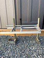Front view of the portable lumber mill metal frame on gravel with a shed background.