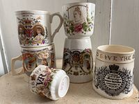 Photo showing six ceremonial ceramic cups with royal portraits and inscriptions, stacked and arranged on a windowsill.