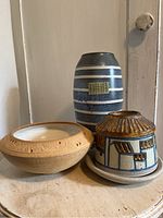 Three studio pottery pieces arranged on a wooden surface showing the vase, lidded pot, and bowl.