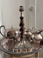 Vintage silver-plated tableware set arranged on the serving tray showing teapot, creamer, sugar bowl, and candlestick with twisted oak shaft.