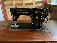 Front side view showing vintage black Singer 306K sewing machine mounted in wood cabinet with machine bed and arm visible