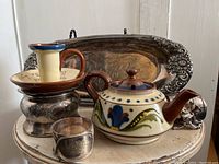 Wide shot showing the collection of items on a small table including the teapot, candleholder, silver plate tray, shaving cup, and napkin rings.