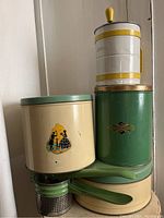 Vintage kitchen tins, flour sifter, and potato ricer stacked showing colors and condition