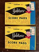 Photo of two unopened vintage Yahtzee score pad boxes showing front design and character with graduation cap and bow tie.