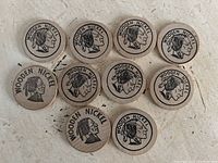 Photo showing 10 wooden nickels arranged on a surface, each with the Native American profile and text 'WOODEN NICKEL'.