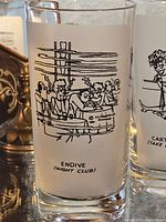 Tall clear glass with black comic drawing of people at a night club titled Endive (Night Club) by Richard Taylor.