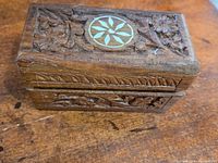 Top and front view of the small rectangular wooden box showing intricate floral carvings and circular inlaid design on the lid.