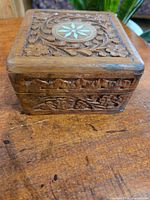 Front view of the medium-sized wooden stash box showing carved floral and geometric details on the lid and sides.