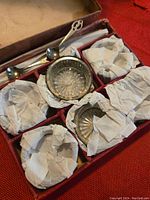 Overview of the vintage box containing multiple silver salt cellars wrapped in tissue paper and small silver spoons.