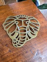 Brass elephant trivet showing smooth front side with cutout elephant head pattern resting on a wooden table.