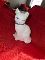 Frontal view of the Fenton cat figurine showing the white opalescent glass and blue rhinestone collar.