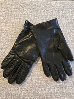 Pair of black leather gloves laid out on grey fabric surface showing both gloves, highlighting the leather texture and stitch detail.