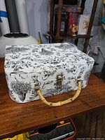 Front and angled view showing the black and white toile fabric design and bamboo handle with metal clasps.