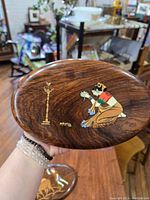 Close-up of the oval wood plaque showing the woman praying inlaid artwork and lamp.