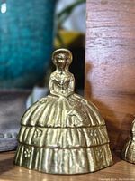 Front view of the vintage brass bell shaped as a Victorian lady with a wide dress and bonnet.