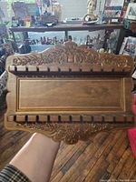 Front view of wooden silverware wall hanger showing decorative carved floral pattern and multiple slots for silverware.