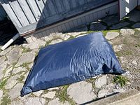 Photo of large blue bean bag chair laid on stone surface outside, showing overall condition and fabric texture.