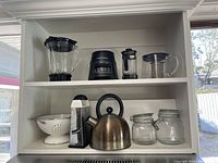 Photo of shelf holding all items described in the lot: blender base with glass jar, stainless steel kettle, French press, glass measuring jug, metal grater, white colander, and glass jars with clamp lids.