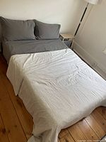 Image showing made double bed with grey fitted sheets, matching pillows and white patterned blanket.