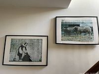 Two framed posters on a wall, left image shows maid holding curtain, right image two cows with graffiti