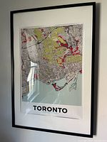 Framed Toronto city map poster with color highlights in green, red, black on white background, displayed on wall.
