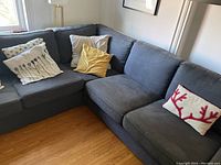 Corner view of L-shaped sectional showing left sofa section and corner module with three throw pillows.