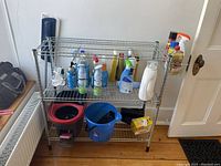 Wide view of metal shelving with assorted cleaning supplies, mop bucket, blue plastic bucket, and iron.