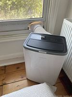 Portable air conditioner set up with white flexible exhaust hose vented to window with insert.