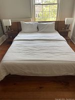 Front view of assembled bed with bedding and pillows, lamps on nightstands