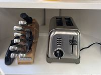 Photo showing stainless steel toaster next to wooden knife block with knives and handheld sharpener